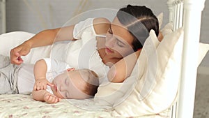 Happy mom is lying with her newborn sleeping baby in bed, she admires the baby.