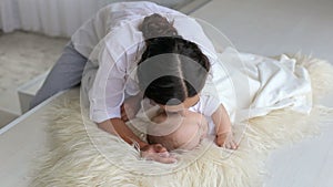 Happy mom is lying with her newborn sleeping baby in bed, gently kisses him.