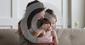 Happy mom playing with daughter blowing soap bubbles at home