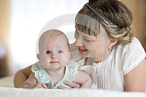 Happy mother playing and hug with newborn baby in bed