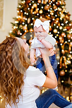 Happy mom playing with little cute baby daughter while sitting near Christmas tree in living room