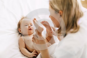 Happy mom plays with her baby on the bed and holds his legs in her hands