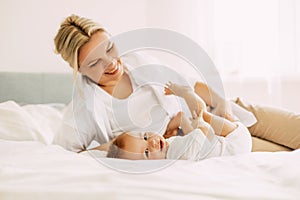 Happy mom plays with her little son lying on the bed, mom and baby relax together. Innocence, unity and family