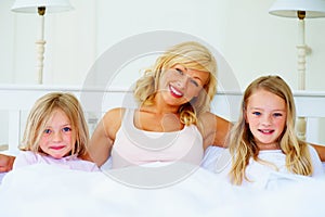 Happy mom, portrait and children relax in bed for holiday, weekend or morning together at home. Mama and daughters smile