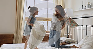 Happy mom and preschool child enjoy pillow fight on bed