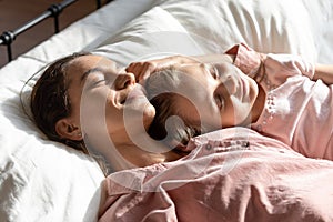 Happy mom relaxing sleeping with little daughter in bed