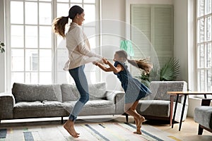 Happy mom and small daughter dancing jumping at home