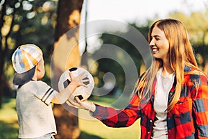 Happy mom and son are playing with a soccer ball while sitting on the green grass in the park. Image of family