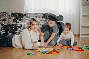 Happy mom and sons sit on floor playing with toy blocks together