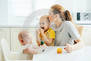 Happy mom spends time with the children in the kitchen feeding them.