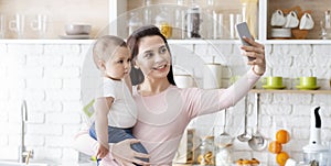 Happy mom taking photo with baby on smartphone at kitchen