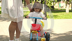 Happy mom teaches little daughter to ride a bike. mother is playing with child outdoors. child learns to ride bicycle