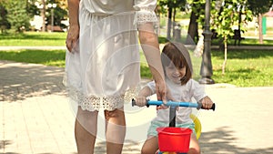 Happy mom teaches little daughter to ride a bike. mother is playing with child outdoors. child learns to ride bicycle
