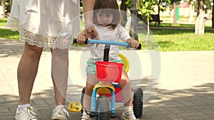 Happy mom teaches little daughter to ride a bike. mother is playing with child outdoors. child learns to ride bicycle