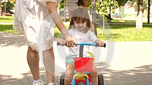 Happy mom teaches little daughter to ride a bike. mother is playing with child outdoors. child learns to ride bicycle