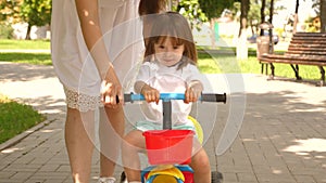 Happy mom teaches little daughter to ride a bike. mother is playing with child outdoors. child learns to ride bicycle