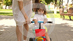 Happy mom teaches little daughter to ride a bike. mother is playing with child outdoors. child learns to ride bicycle