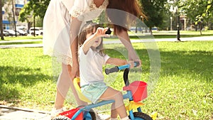 Happy mom teaches little daughter to ride a bike. mother is playing with child outdoors. concept of happy family and