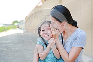 Happy mom whispering a something secret to her little daughter ear. Mother and kid communication concept