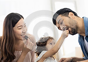 Happy moment family eating chocolate cookie in living room at home. Father Mother and daughter laughing having a good meal in the