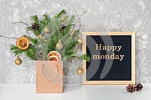Happy Monday text on black letter board and festive bouquet of fir branches with christmas decor in craft package on table.