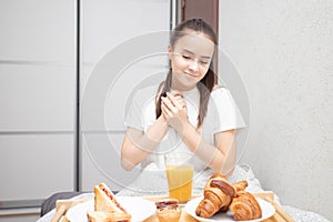 Happy morning. A young woman eats a delicious Breakfast in bed - fresh croissants, coffee, orange juice and muesli with fruit