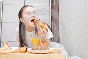 Happy morning. A young woman eats a delicious Breakfast in bed - fresh croissants, coffee, orange juice and muesli with fruit