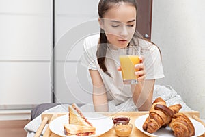 Happy morning. A young woman eats a delicious Breakfast in bed - fresh croissants, coffee, orange juice and muesli with fruit