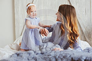 Happy mother and 9 month old baby in matching pajamas playing in bedroom in the morning