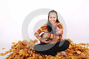 Happy mother and baby boy sitting on maple leaves by pumpkin