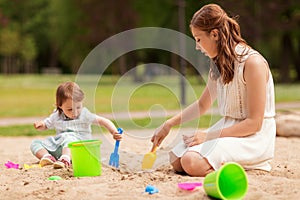 Happy mother and baby girl playing in sandbox