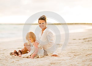 Happy mother and baby girl sitting on the beach