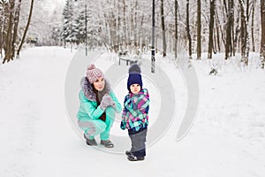 Happy mother and baby girl on the walk in winter snowy forest
