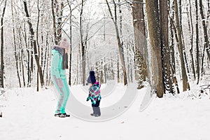 Happy mother and baby girl on the walk in winter snowy forest