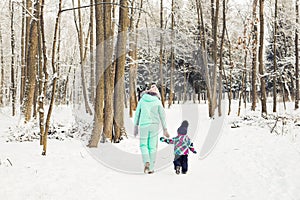 Happy mother and baby girl on the walk in winter snowy forest