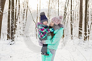 Happy mother and baby girl on the walk in winter snowy forest