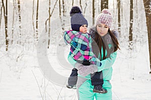 Happy mother and baby girl on the walk in winter snowy forest