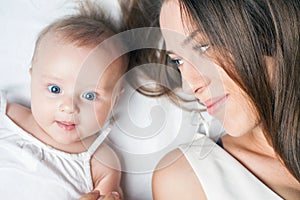 Happy mother with a baby lying on a white bed