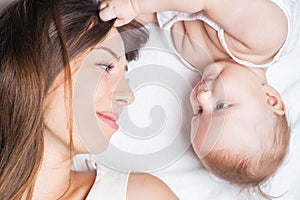 Happy mother with a baby lying on a white bed