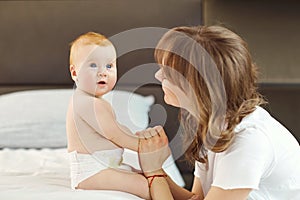 Happy mother with baby sitting on the bed indoors.