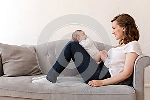 Happy mother with baby sitting on sofa
