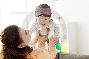 Happy mother with baby wearing pilot hat at home