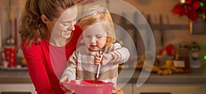 Happy mother and baby whisking dough in christmas kitchen