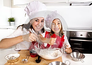 Happy mother baking with little daughter in apron and cook hat with flour dough at kitchen