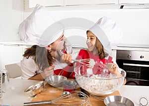 Happy mother baking with little daughter in apron and cook hat with flour dough at kitchen