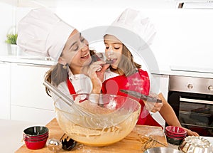 Happy mother baking with little daughter eating chocolate bar used as ingredient while teaching the kid