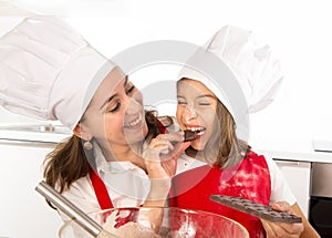 Happy mother baking with little daughter eating chocolate bar used as ingredient while teaching the kid