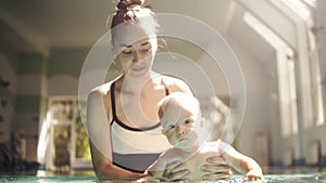 Happy mother in black and white swimming suit with baby son surfing above the water with fun in swimming pool. Healthy