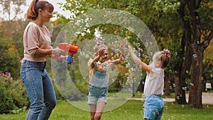 Happy mother blowing soap bubbles with toy gun, little daughters trying to catch