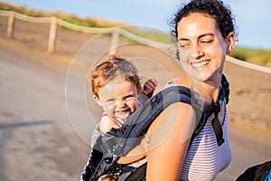 Happy mother carrying a smiling baby on her back in a baby carrier outdoors